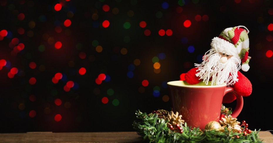 santa and a cup of coffee christmas lights in background and wreath beneath cup