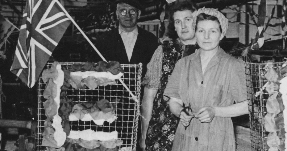 black and white photograph of mill workers in factory with union flags and decorations