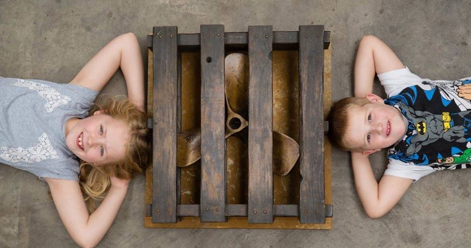 children at museum lieign on floor looking up at camera with propeller in between them