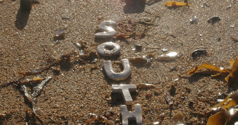 sand on a beach with stones, seaweed and silver letters spelling south sand on a beach with stones, seaweed and silver letters spelling south